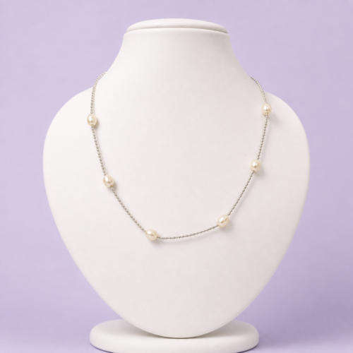 Silver-tone tin cup pearl station necklace with seven oval ivory pearls displayed on white bust against lavender background