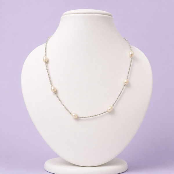 Silver-tone tin cup pearl station necklace with seven oval ivory pearls displayed on white bust against lavender background