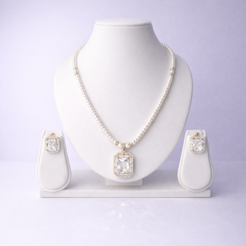 Gold-tone pearl necklace set with emerald-cut crystal pendant and matching crystal stud earrings displayed on white bust